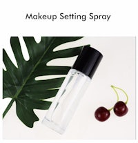 a bottle of makeup setting spray with a cherry next to it