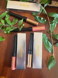 three lip glosses sitting on a wooden table